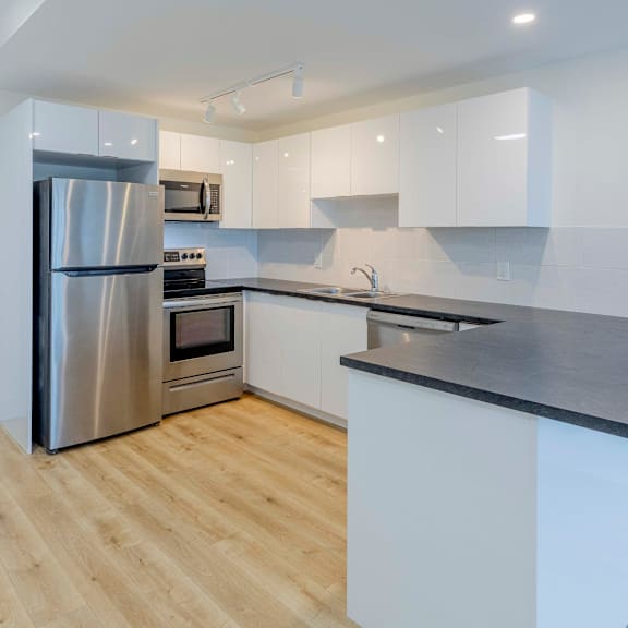 a modern kitchen with a stainless steel refrigerator and wooden flooring.