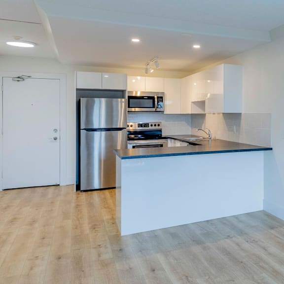 a modern kitchen with a stainless steel refrigerator and wooden flooring.
