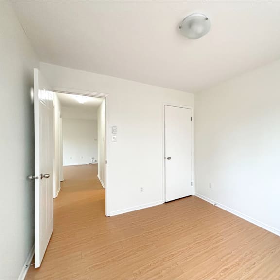a room with white walls and wooden flooring with a door on the left and a window on the right.