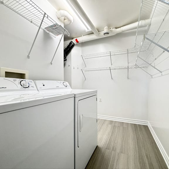 a white washing machine in a laundry room with a fan and shelving above it.