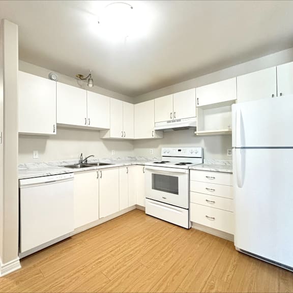 a white kitchen with wooden floors and white appliances.