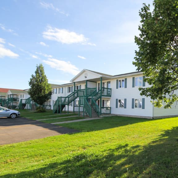 a white building with green railings and a tree in front.