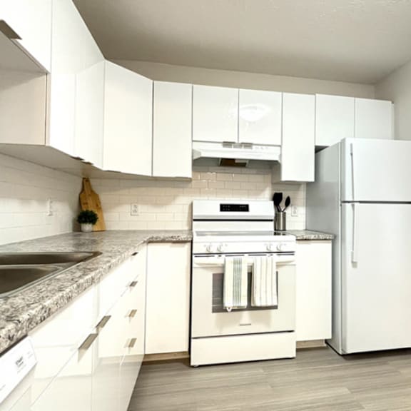 a white kitchen with a refrigerator, oven, and sink.