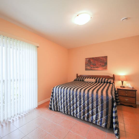 a bedroom with a bed, nightstand, and window with blinds.