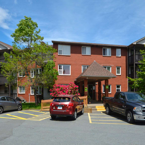 a red car is parked in a parking lot in front of a brick building.