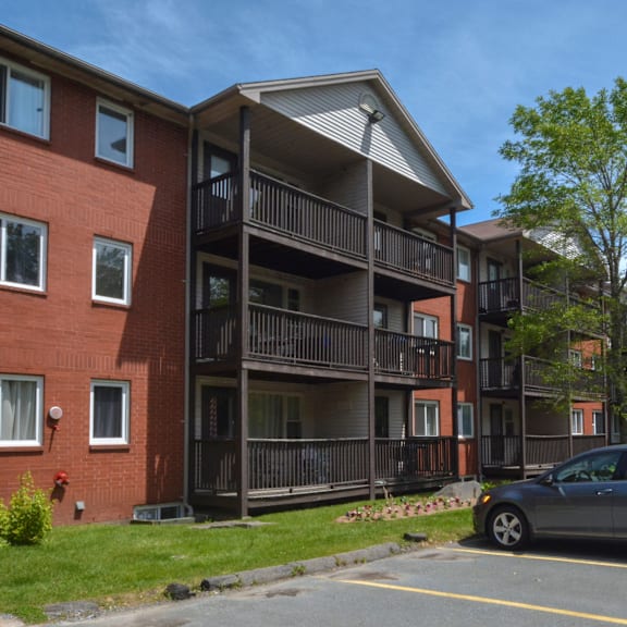 a grey car is parked in a parking lot in front of a red brick building with a balcony.