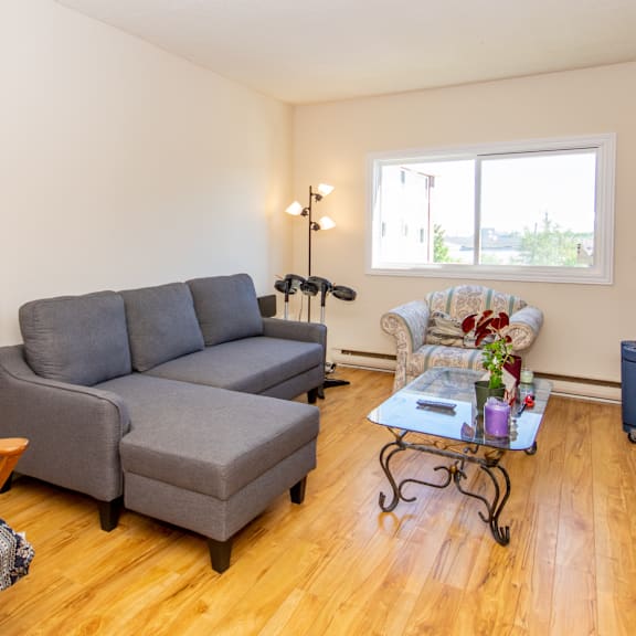 a grey couch sits in a living room with a fan and a chair.