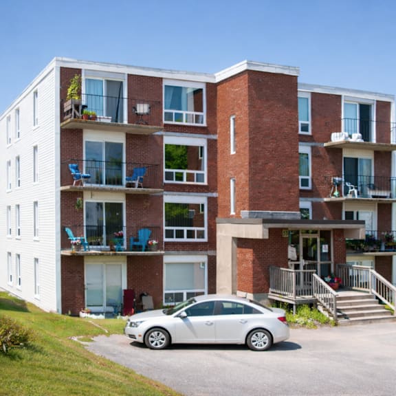 a white car is parked in front of a red brick apartment building.