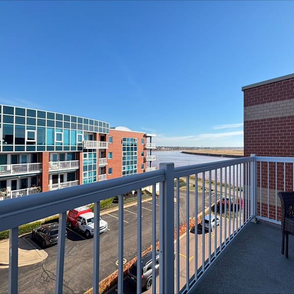 a balcony with a chair and a railing overlooking a parking lot and buildings.