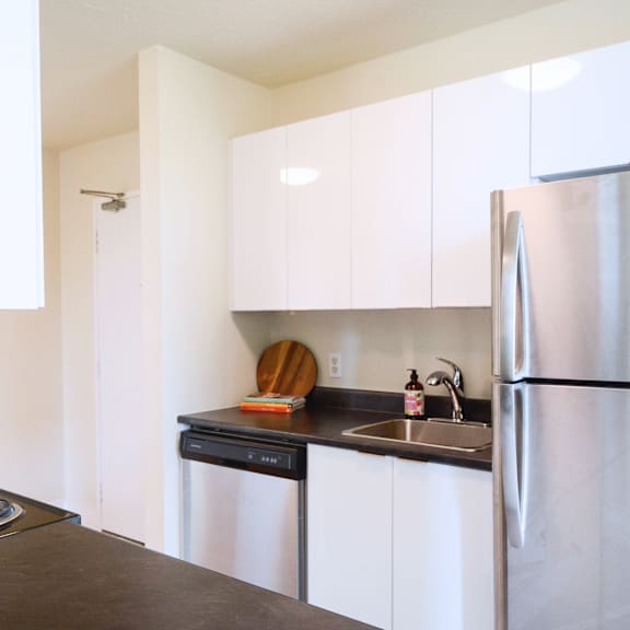 a kitchen with a stainless steel refrigerator and black countertop.