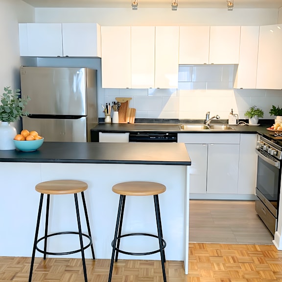 a kitchen with white cabinets and a black countertop with a refrigerator, stove, and two bar stools.