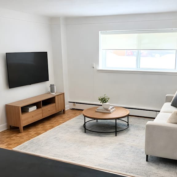 a living room with a grey couch, a wooden coffee table, a television, and a window with blinds.