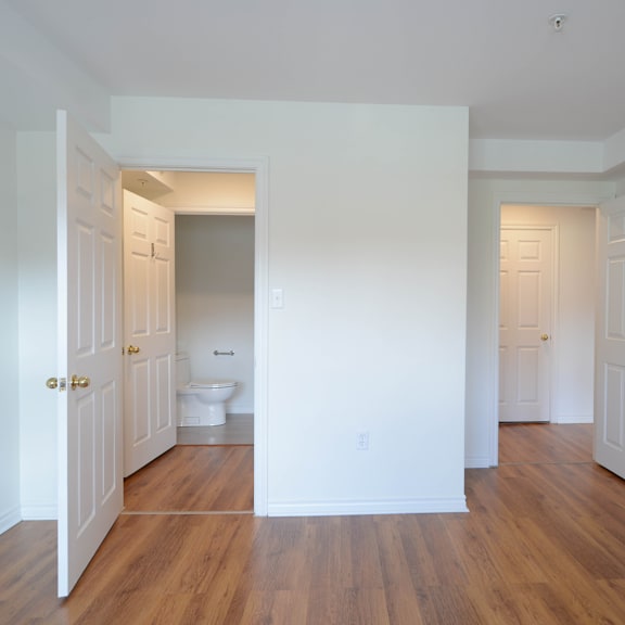 a white bathroom with wood floors and a toilet in the middle.