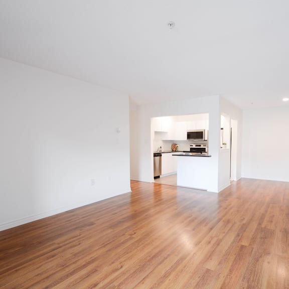 a room with wooden floors and a kitchen area in the background.
