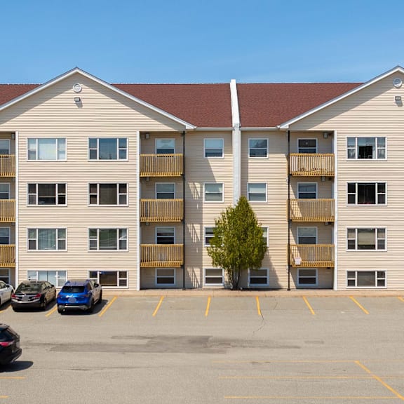 a parking lot in front of a tan apartment building with cars parked.