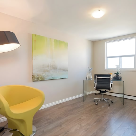 a yellow chair is in the corner of a room with a desk and a painting on the wall.