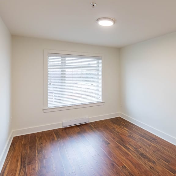a room with wooden floors and a window with blinds.