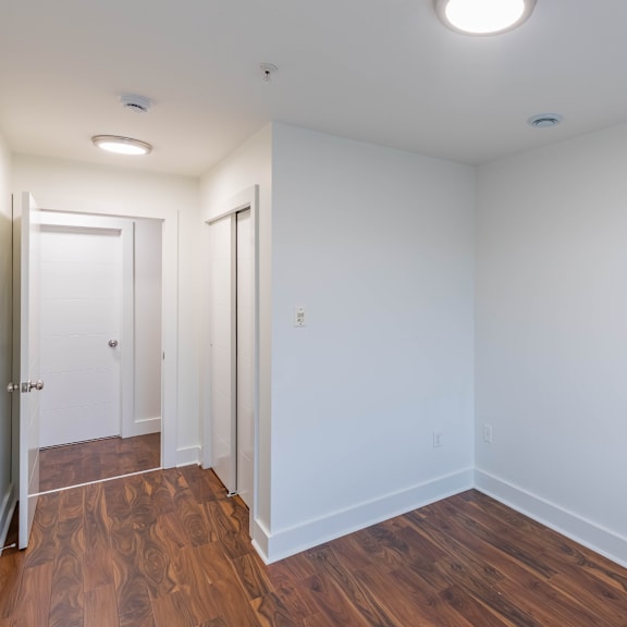 a room with white walls and wooden flooring with a door on the left.