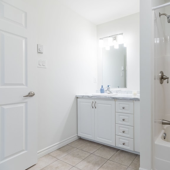 a white bathroom with a sink, mirror, and bathtub.