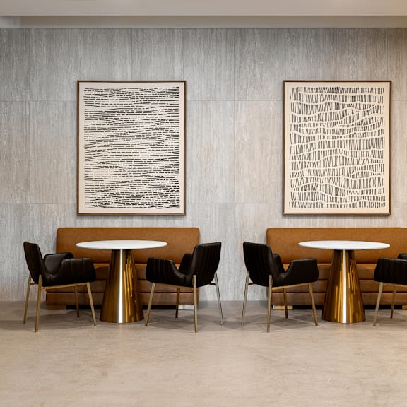 two artworks hang on a wall above a table with chairs.