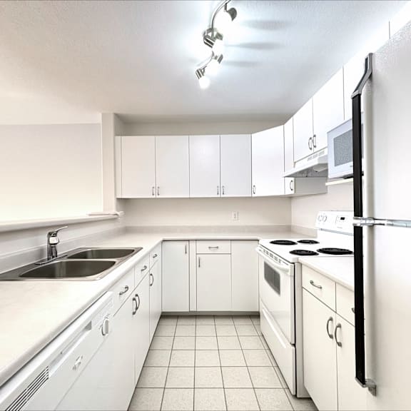 a white kitchen with a refrigerator, sink, and oven.