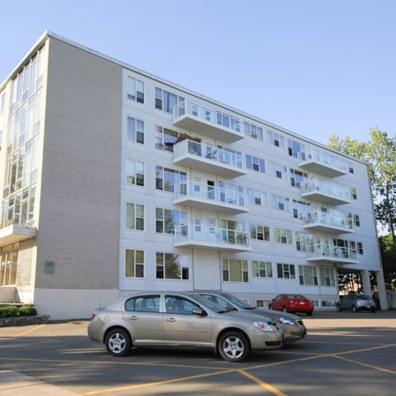 a silver car is parked in a parking lot in front of a white building with balconies.