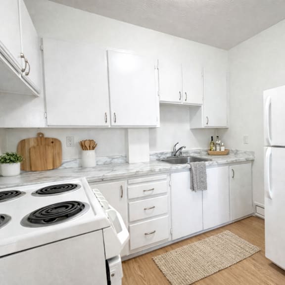 a white kitchen with a stove, sink, and refrigerator.