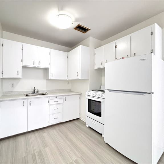 a white kitchen with a refrigerator, sink, and cabinets.