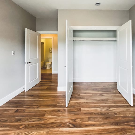 a room with a wooden floor and white walls with two open doors.