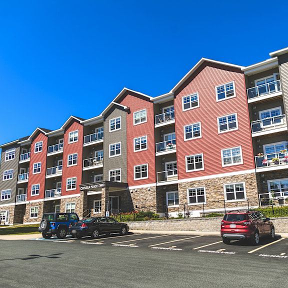 a parking lot in front of a multi-story apartment building with cars parked.