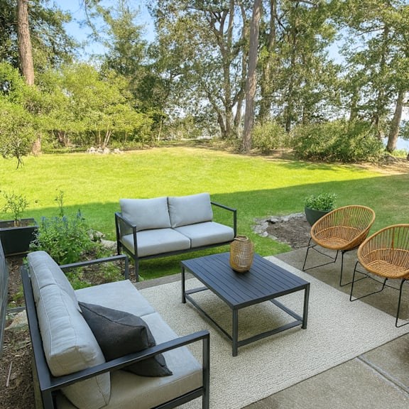 a patio with a black table and chairs with a view of a grassy field and trees.