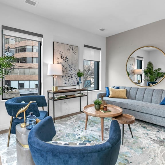 a living room with a grey couch, blue armchair, and a round mirror.