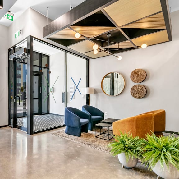 a modern waiting area with a glass door, a blue chair, a brown chair, and a potted plant.