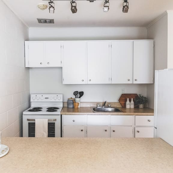 a white kitchen with a stove, sink, and cabinets.