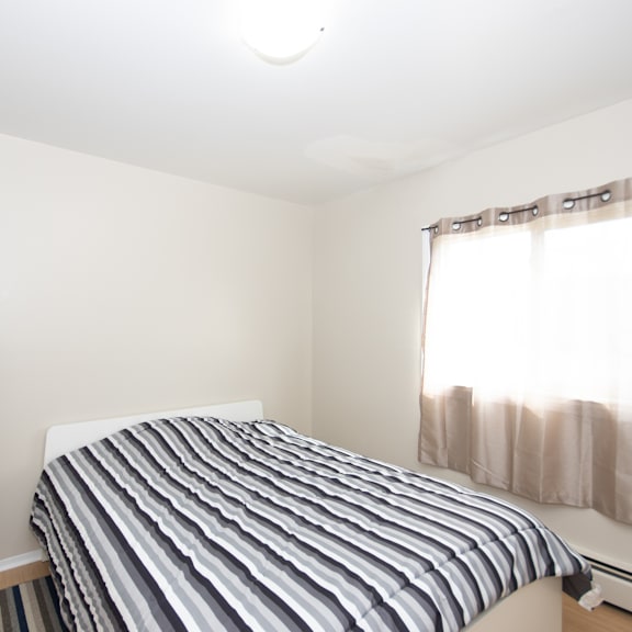 a bed with a striped comforter sits in a room with a window.