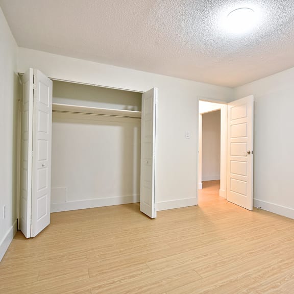 a room with a white wall and a wooden floor with two open doors.