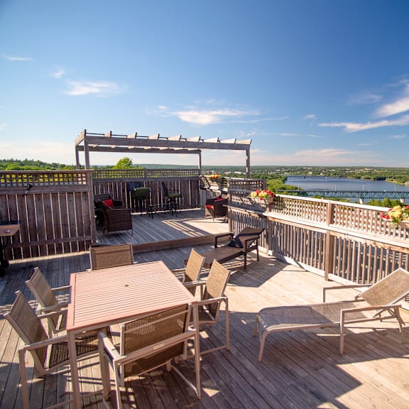a wooden deck with chairs and a table overlooking a river.