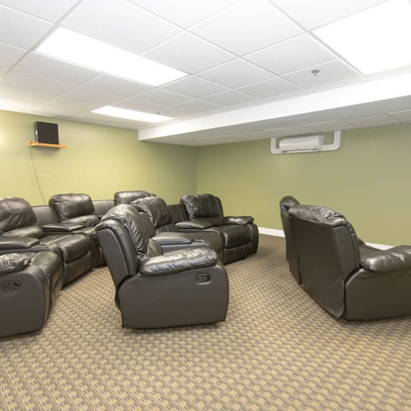 a room with a carpeted floor and rows of black leather recliner chairs.