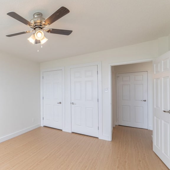a room with a ceiling fan and three white doors.