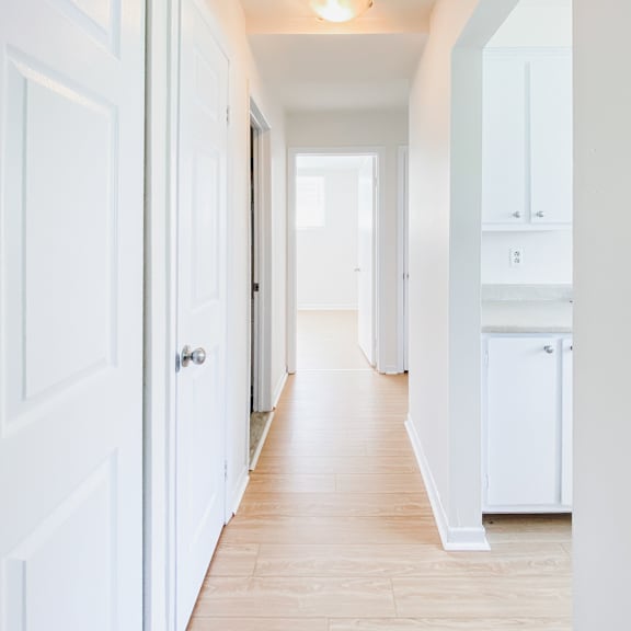 a long hallway with white doors and cabinets.