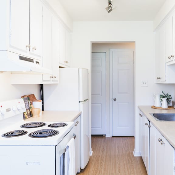 a white kitchen with a stove, sink, and cabinets.