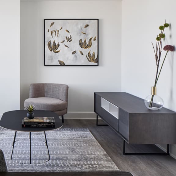 a grey chair sits in front of a painting and a coffee table with a vase on top.