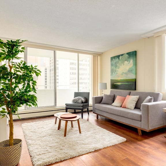a living room with a grey couch, a wooden coffee table, and a large window with a view of a city skyline.