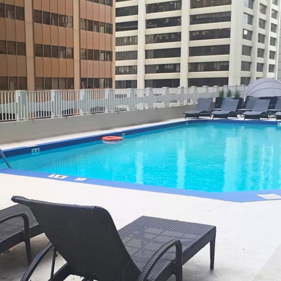 a pool with chairs around it and buildings in the background.