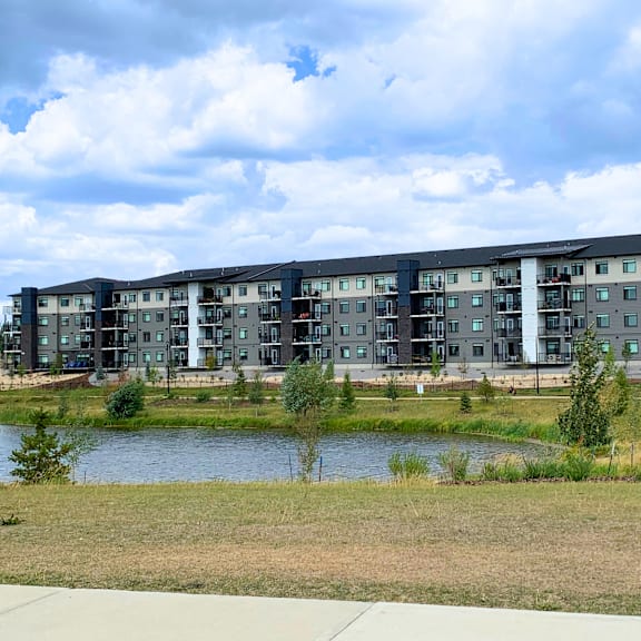 a modern apartment complex with a lake in front.