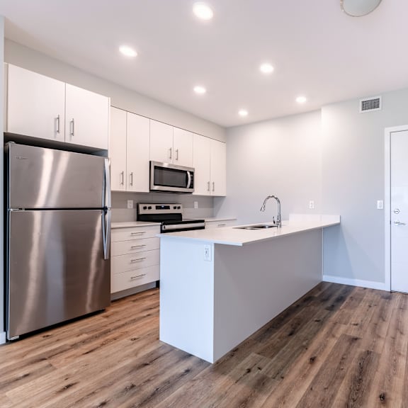 a modern kitchen with a stainless steel refrigerator and wooden flooring.