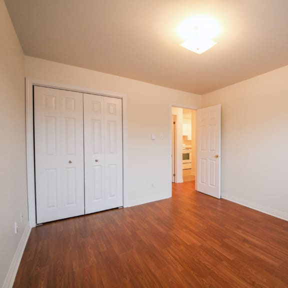 a room with white walls and wooden floors has two white doors.