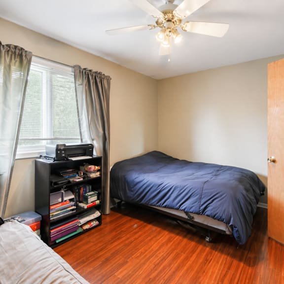 a bedroom with a bed, a ceiling fan, and a bookshelf.