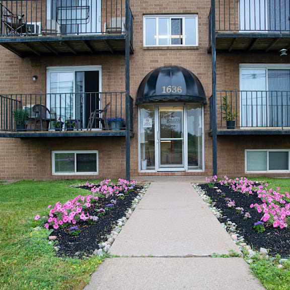 the front of apartment building number 1636 with a walkway and flower beds.