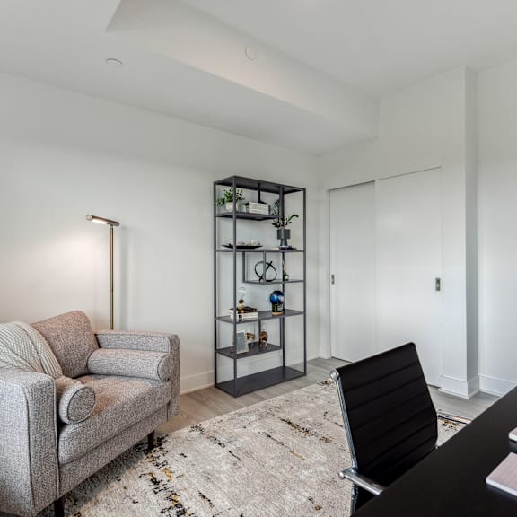 a living room with a grey couch, a black chair, and a bookshelf with various items.